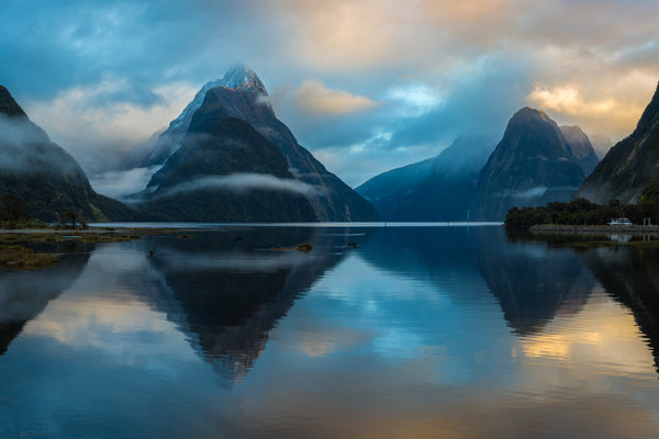 Tranquil calm waters at high tide as the sky softly changes from hues of blue to yellow as the morning sun begins to rise above the Fiords mountain tops.  Shot taken in Milford Sound, Fiordland.