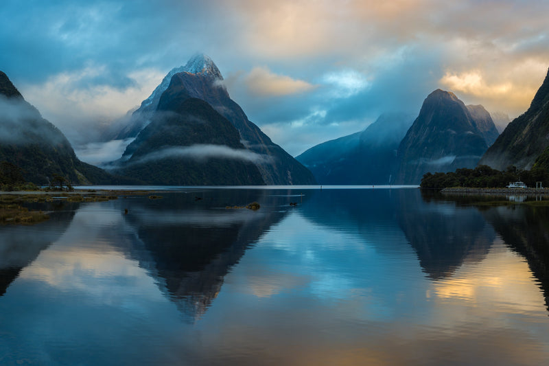 Tranquil calm waters at high tide as the sky softly changes from hues of blue to yellow as the morning sun begins to rise above the Fiords mountain tops.  Shot taken in Milford Sound, Fiordland.