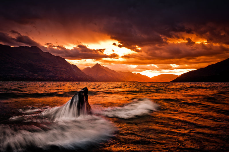 The sun drops below the horizon behind Walter Peak and Lake Wakatipu on a stormy summers evening.
