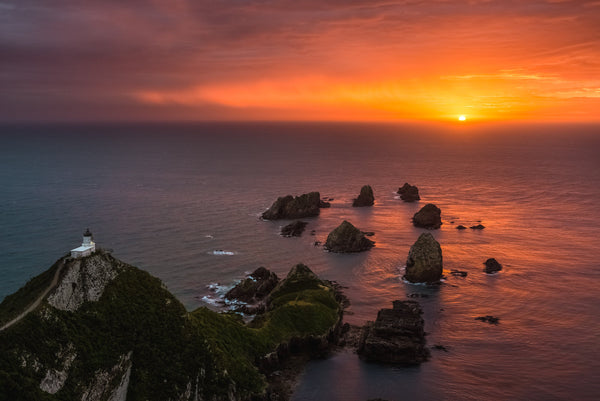 A rainy, stormy skied morning leads to a beautiful golden sky as the sun rises over the Pacific Ocean to the East at Nugget Point, Catlin Coast.