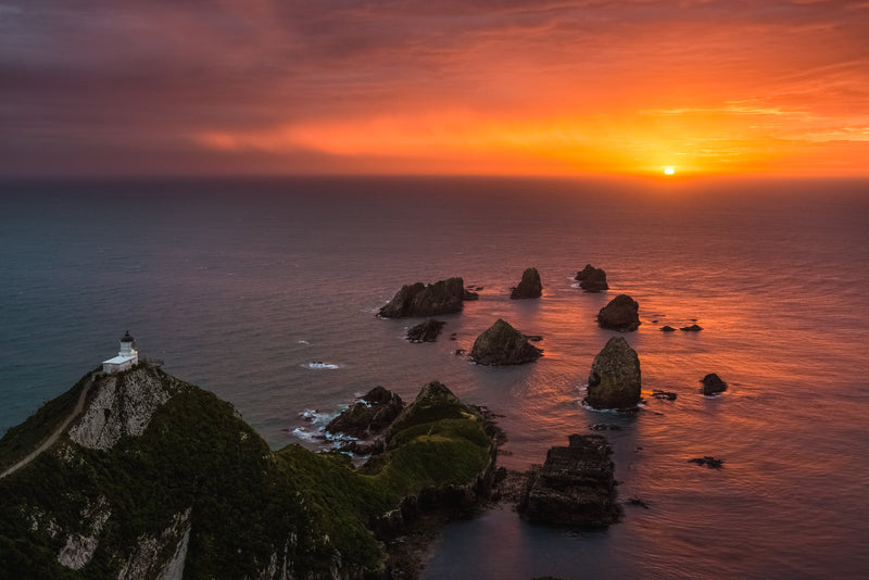 A rainy, stormy skied morning leads to a beautiful golden sky as the sun rises over the Pacific Ocean to the East at Nugget Point, Catlin Coast.