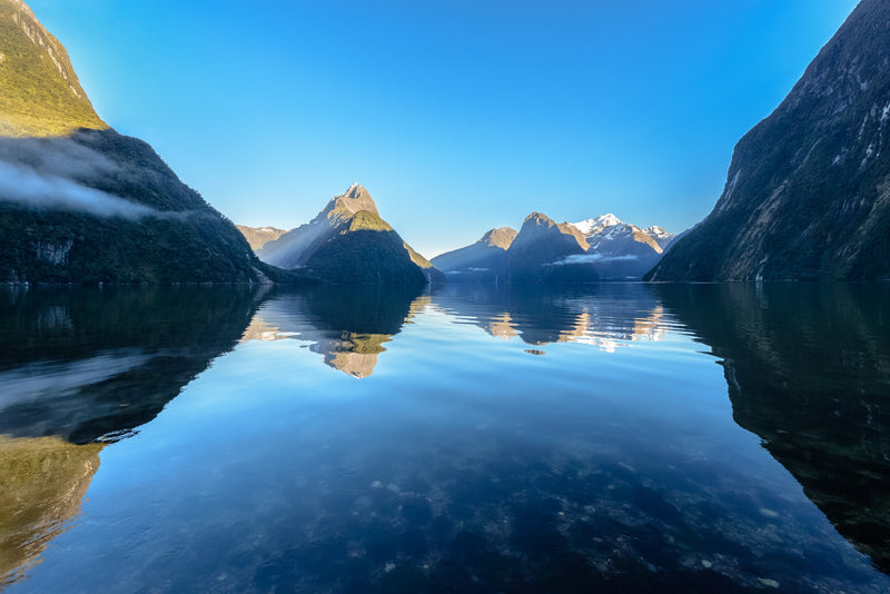 A calm morning as the first sunlight of the day strikes the peaks surrounding Milford Sound, Fiordland.