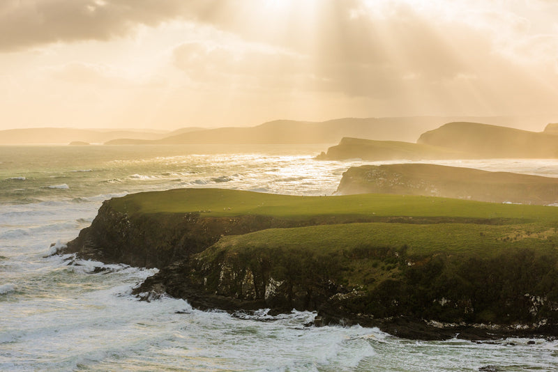 As the sea swell pounds the coastal cliffs, the skies are filled with sunrays that break through the stormy skies.